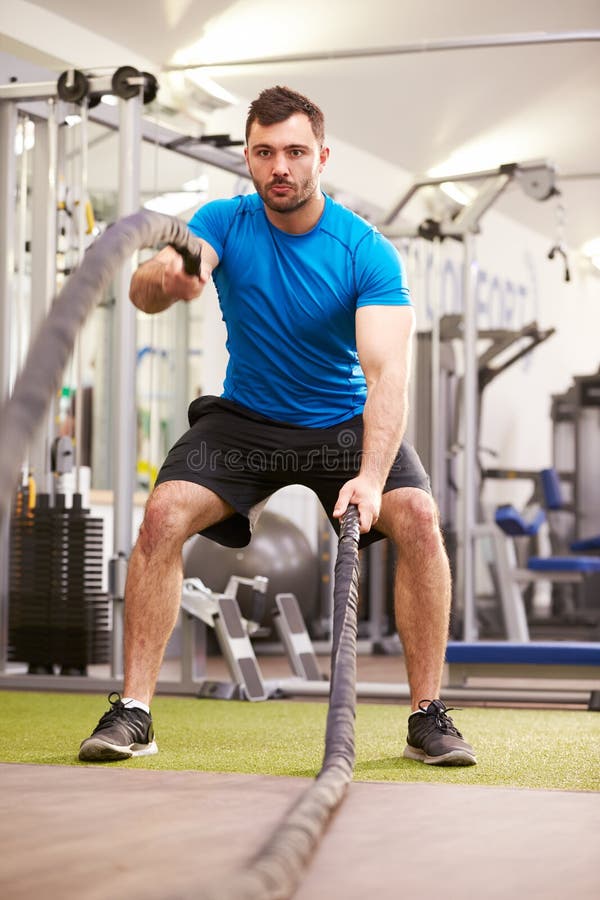 Young man working out with battle ropes at a gym, vertical