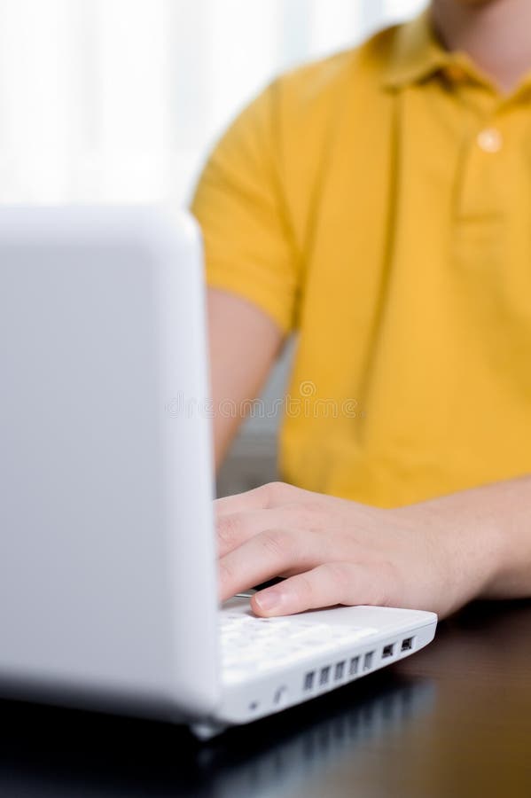 Young man in yellow shirt types on notebook royalty free stock images