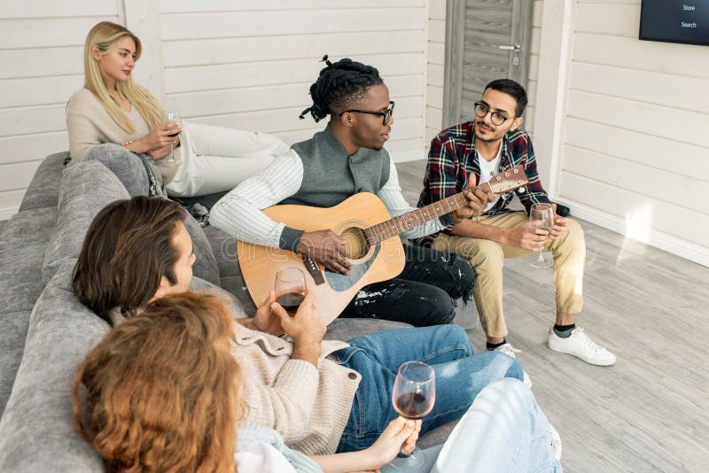 Young man with guitar singing for his friends sitting around him on couch stock photography Young man with guitar singing for his friends sitting around him on couch stock photography