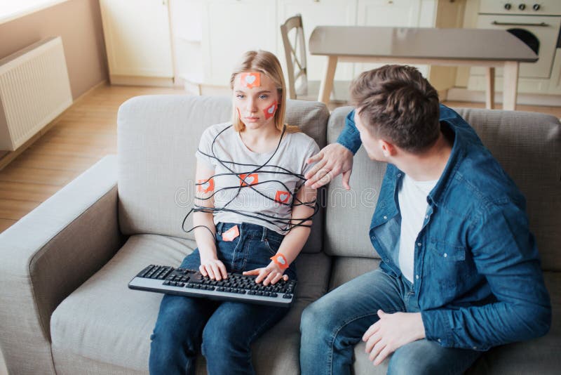 Young man and woman have social media addiction. Sitting on sofa. Hostages. Emotionless woman on sofa. Worried man stock photo Young man and woman have social media addiction. Sitting on sofa. Hostages. Emotionless woman on sofa. Worried man stock photo