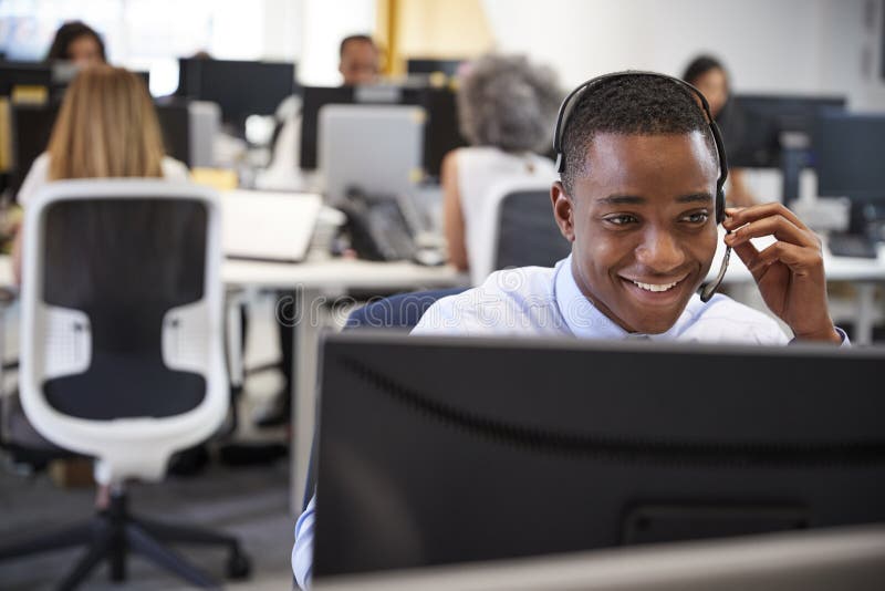 Young man working at computer with headset in busy office royalty free stock photography Young man working at computer with headset in busy office royalty free stock photography