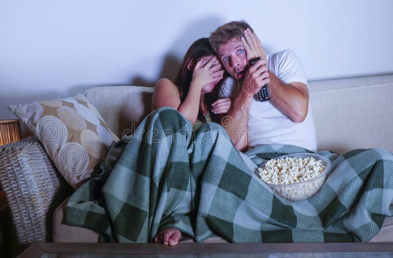 Young mixed race attractive couple with Asian Korean woman and white man enjoying together watching television horror movie scared royalty free stock image Young mixed race attractive couple with Asian Korean woman and white man enjoying together watching television horror movie scared royalty free stock image