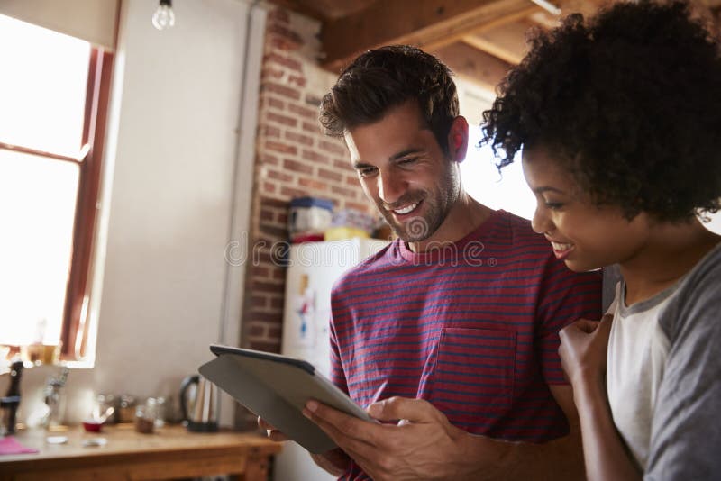 Young mixed race couple using tablet in kitchen, close up stock photography