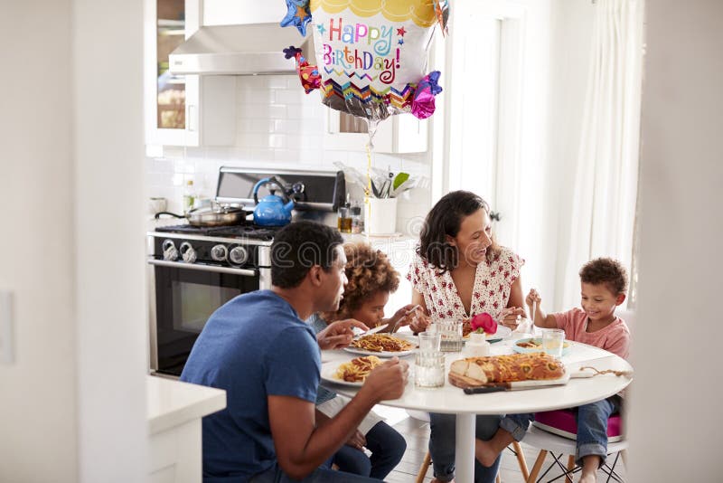 Young African American family having a birthday meal together at the table in their kitchen, seen from doorway stock photography Young African American family having a birthday meal together at the table in their kitchen, seen from doorway stock photography
