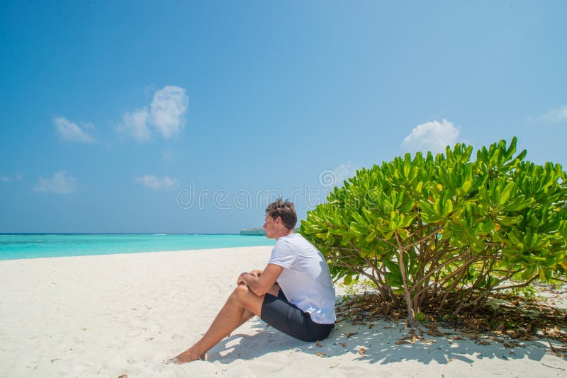 Young model man in white t-shirt sitting on sandy beach at tropical island luxury resort. In Maldives royalty free stock images Young model man in white t-shirt sitting on sandy beach at tropical island luxury resort. In Maldives royalty free stock images
