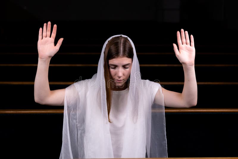 A young modest girl with a handkerchief on her head is sitting in church and praying. The concept of religion, prayer, worship