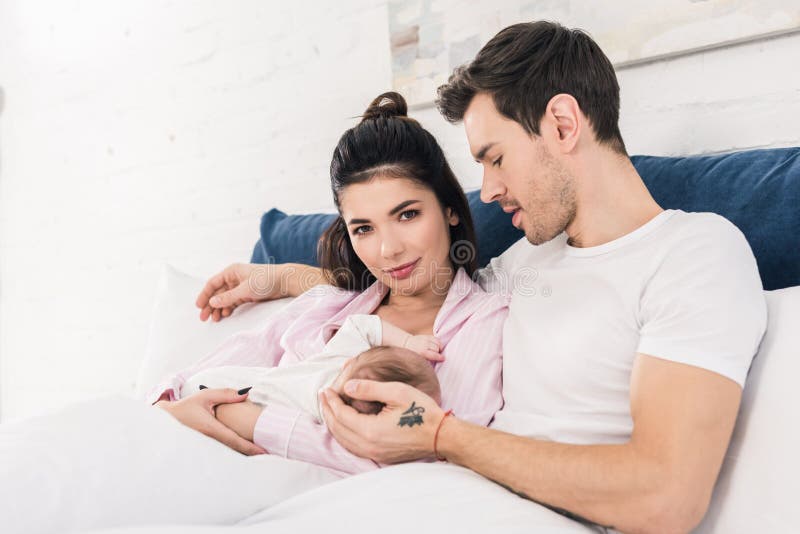 Young Mother Breastfeeding Little Baby with Husband Near by on Bed Stock  Photo - Image of childhood, background: 155844460