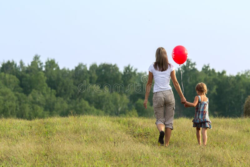 Mother and daughter going to mowed grass. View from back. Mother and daughter going to mowed grass. View from back.