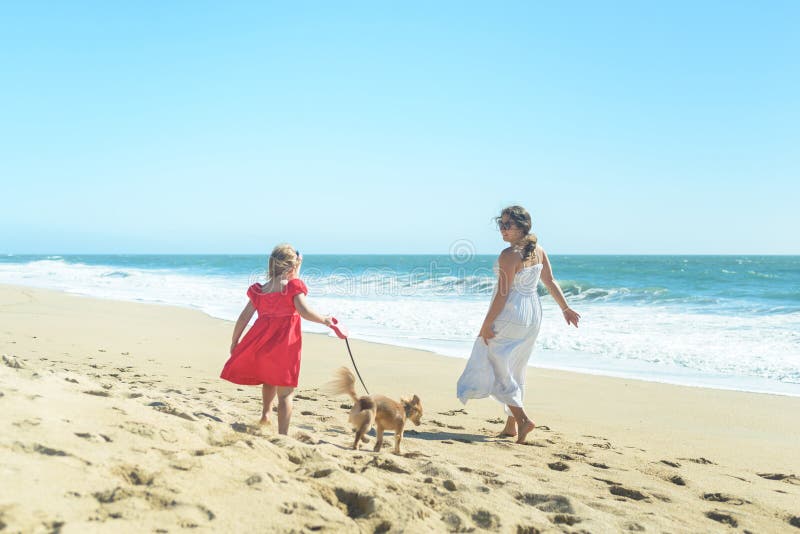 Young mother with girl in red dress and dog on the beach