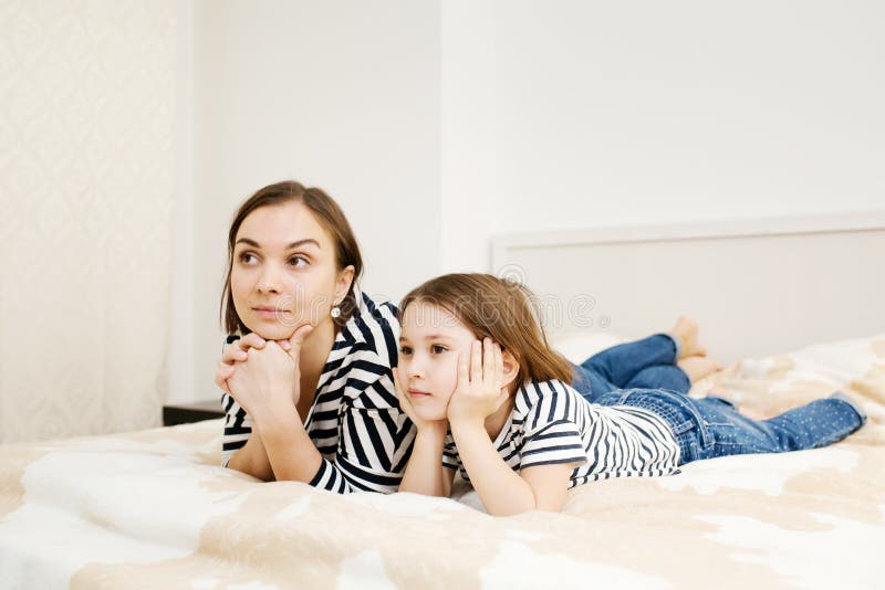 Young mother and her daughter child lying on bed in bedroom and watching tv together royalty free stock image Young mother and her daughter child lying on bed in bedroom and watching tv together royalty free stock image