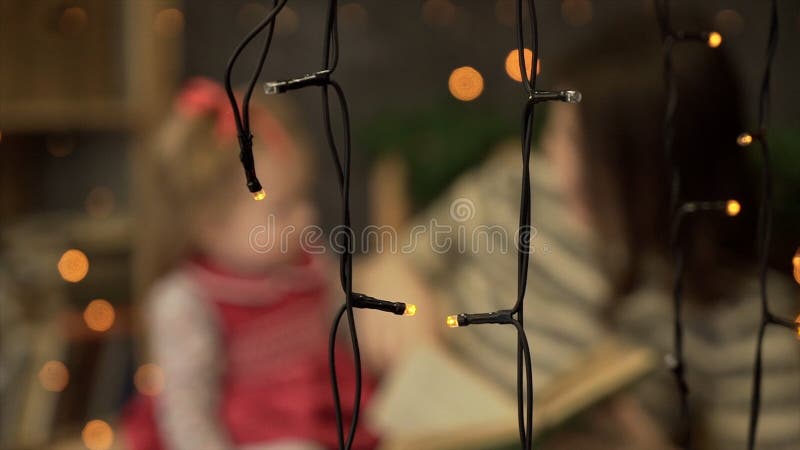 Young mother with little daughter reading book at home. Mom and little daughter playing on background of garlands. Blur royalty free stock photography Young mother with little daughter reading book at home. Mom and little daughter playing on background of garlands. Blur royalty free stock photography