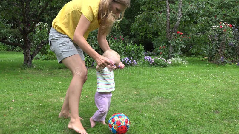 Young mother play with baby girl with ball in summer garden. 4K