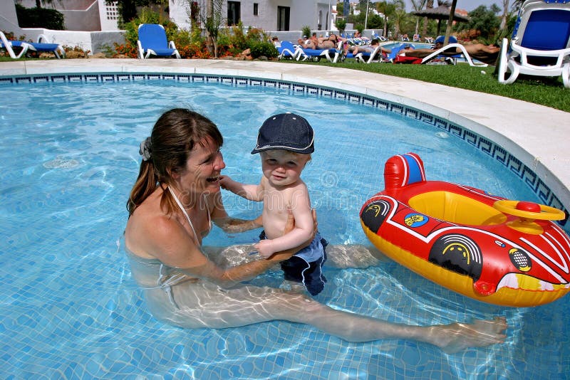 Young mother playing in children s swimming pool with toddler son and inflatable boat.