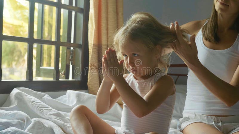 Young mother sits on the bed and combing her daughter. stock photos Young mother sits on the bed and combing her daughter. stock photos