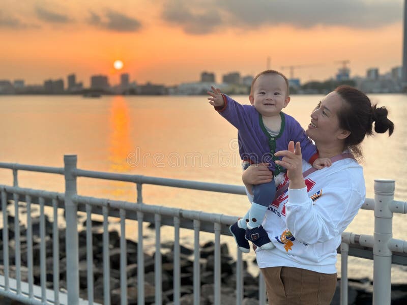 A young mother standing near the quay railing holding her son in her arms.