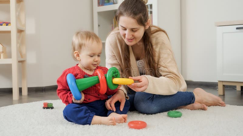 Young mother teaching her little baby son building colorful toy pyramid at home. Baby development, child playing games, education