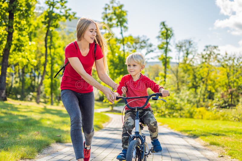 Young mother teaching her son how to ride a bicycle in the park stock photo...