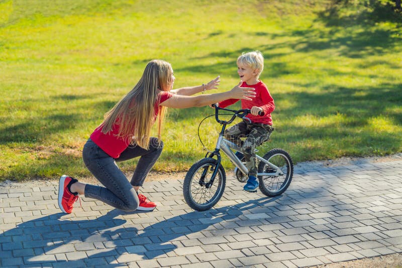 Young mother teaching her son how to ride a bicycle in the park. 