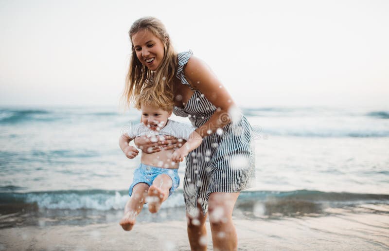 Young mother with a toddler boy standing on beach on summer holiday, having fun.