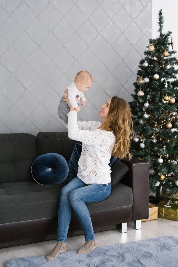 Mother in a white sweater and jeans sits on the couch near the Christmas tree and smiles at her young son. A young mother in a white sweater and jeans sits on stock photography Mother in a white sweater and jeans sits on the couch near the Christmas tree and smiles at her young son. A young mother in a white sweater and jeans sits on stock photography