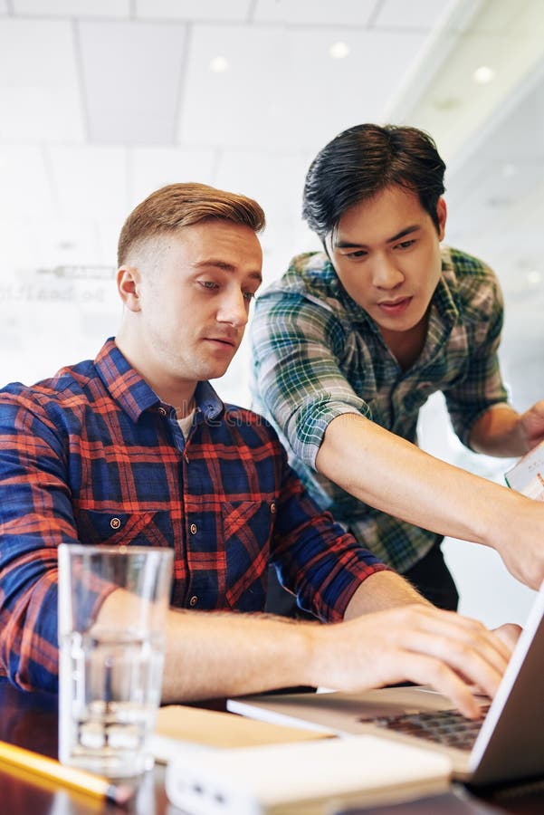 Developers working on mobile app. Young multi-ethnic software developers discussing programming code on laptop screen