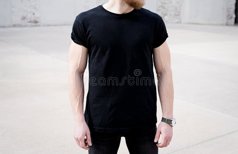 Young muscular bearded man wearing black tshirt and jeans posing in center of modern city. Empty concrete wall on the stock photos Young muscular bearded man wearing black tshirt and jeans posing in center of modern city. Empty concrete wall on the stock photos