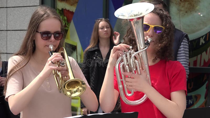 Young musician girls play wind instruments in street public event.