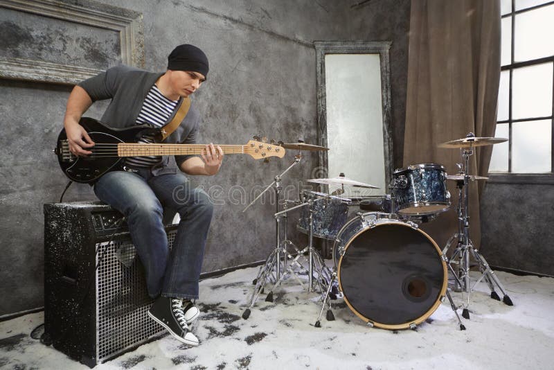 Young musician plays bass electric guitar sitting on amplifier