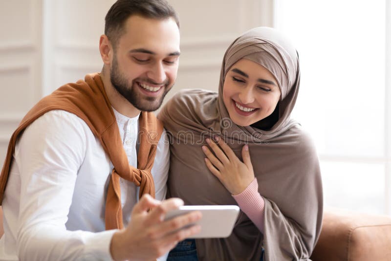 Muslim Couple Using Smartphone and Laughing Sitting in Living Room Stock  Image - Image of modern, indoor: 205027711