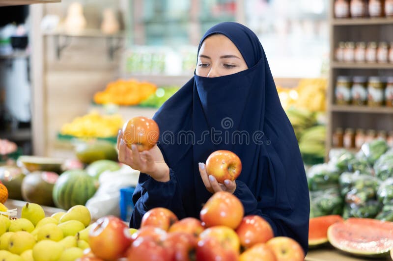 Young Muslim woman in niqab choosing apples in store