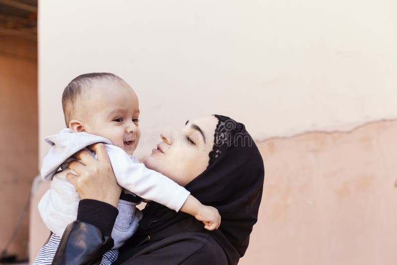 Young Muslim woman in hijab holding her 1-year-old baby boy, hugging and kissing. Happy Muslim mother in abaya clothing kiss and stock photo Young Muslim woman in hijab holding her 1-year-old baby boy, hugging and kissing. Happy Muslim mother in abaya clothing kiss and stock photo