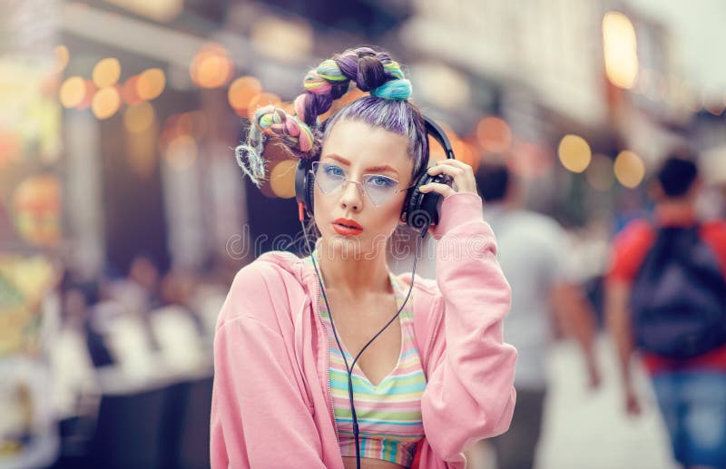 Young nonconformist girl listening music in headphones on the crowded streets. Blurred urban background. Vanguard fashion. stock photography Young nonconformist girl listening music in headphones on the crowded streets. Blurred urban background. Vanguard fashion. stock photography