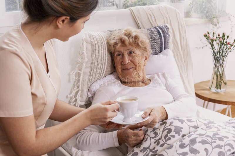 Young nurse serves tea to an elderly lady in a private nursing home