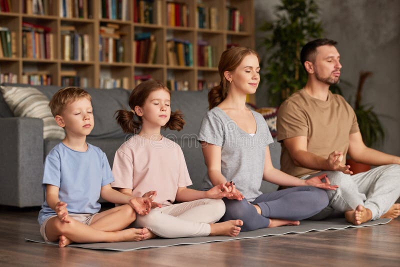 Father, mother and two kids sitting in lotus pose on floor and meditating with closed eyes