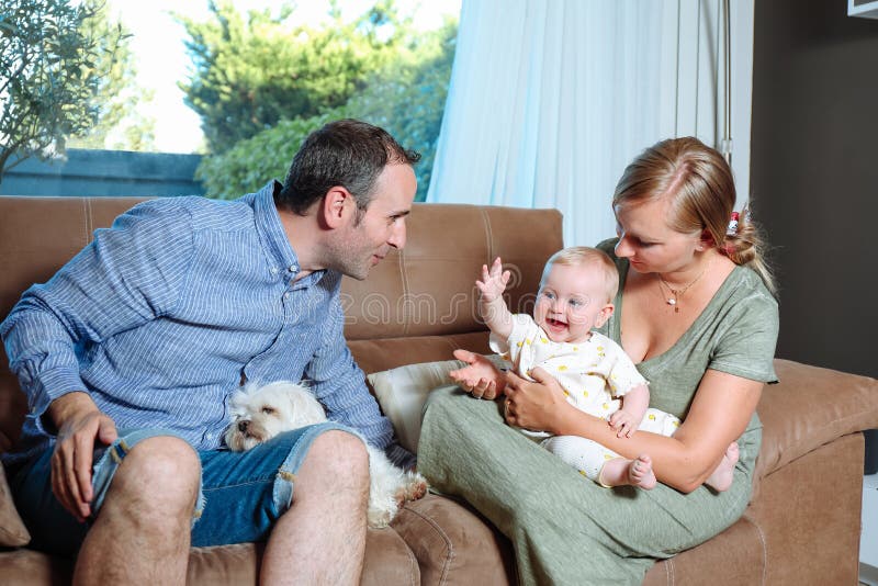 Young parents sitting on the sofa with their cheerful baby and a dog stock photo Young parents sitting on the sofa with their cheerful baby and a dog stock photo