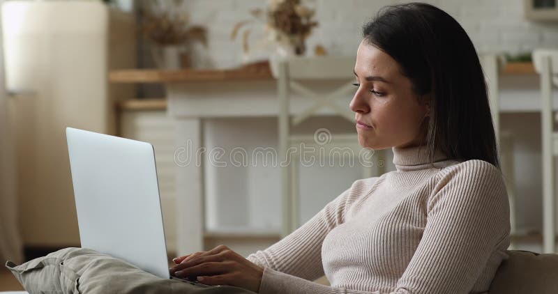 Young pensive woman sit on sofa working on laptop