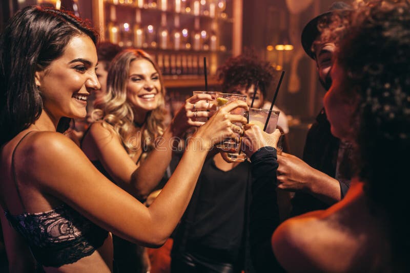 Group of young people with cocktails at nightclub. Best friends partying in a pub and toasting drinks.