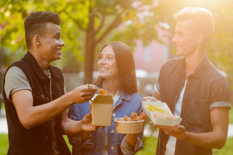 Young people are eating to-go food and talking. Summer weekend with company of friends. Young people are eating to-go food and talking. Summer weekend with company of friends.