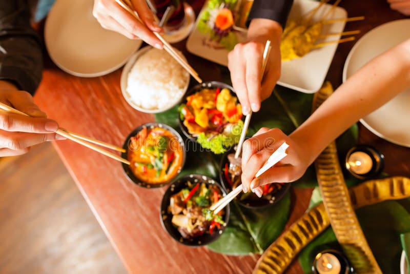 Young people eating in a Thai restaurant, they eating with chopsticks, close-up on hands and food. Young people eating in a Thai restaurant, they eating with chopsticks, close-up on hands and food