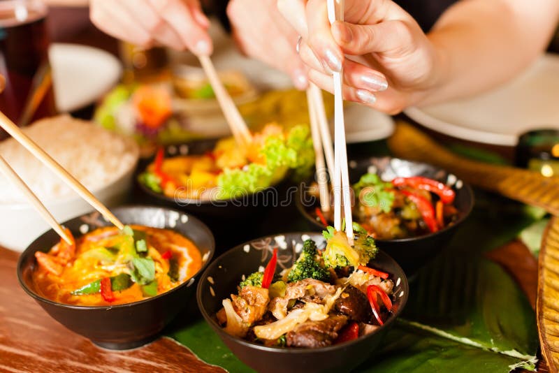 Young people eating in a Thai restaurant, they eating with chopsticks, close-up on hands and food. Young people eating in a Thai restaurant, they eating with chopsticks, close-up on hands and food