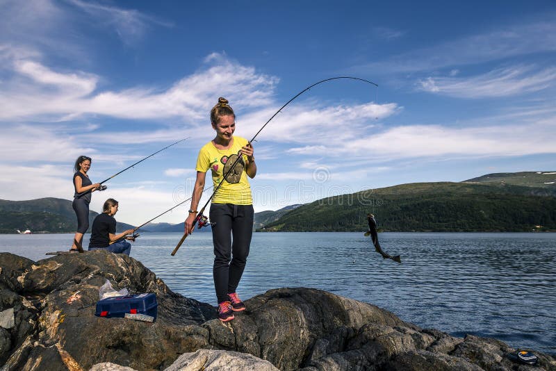 Young people are fishing on the rocks next to the fjord, Norway