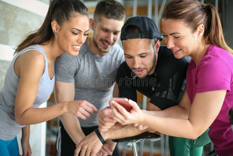 Young people in gym. Friends workout in gym and using smart phone. Watching something on phone.