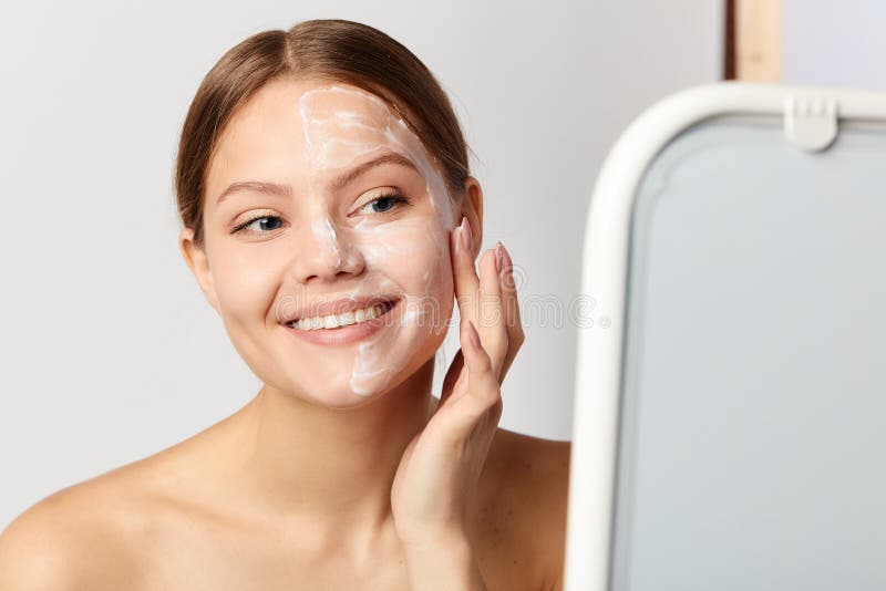 Young positive girl applying cream on face