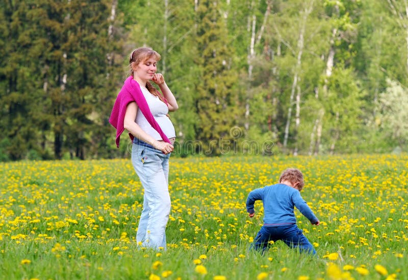 Young pregnant woman and her son in field of dandelion