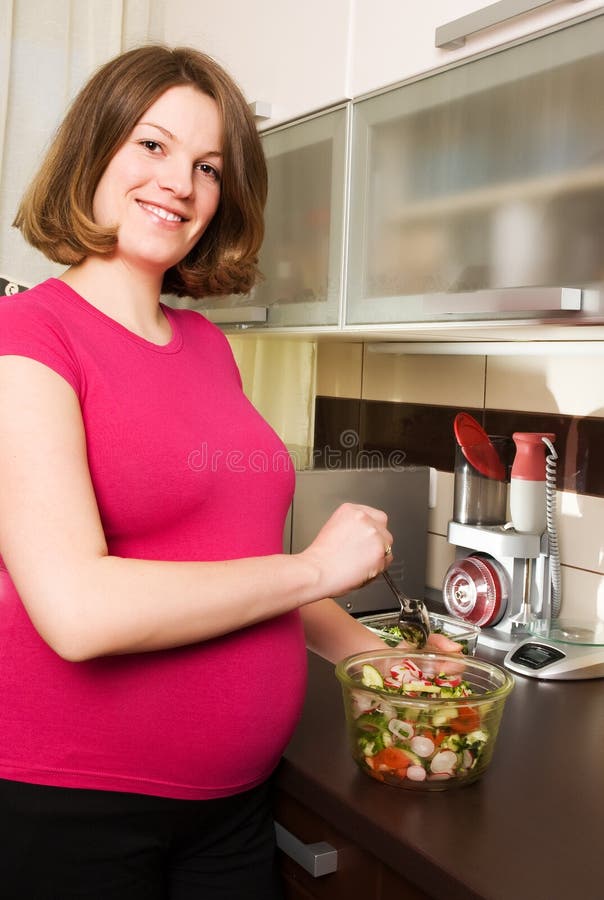 Young pregnant woman in kitchen making salad