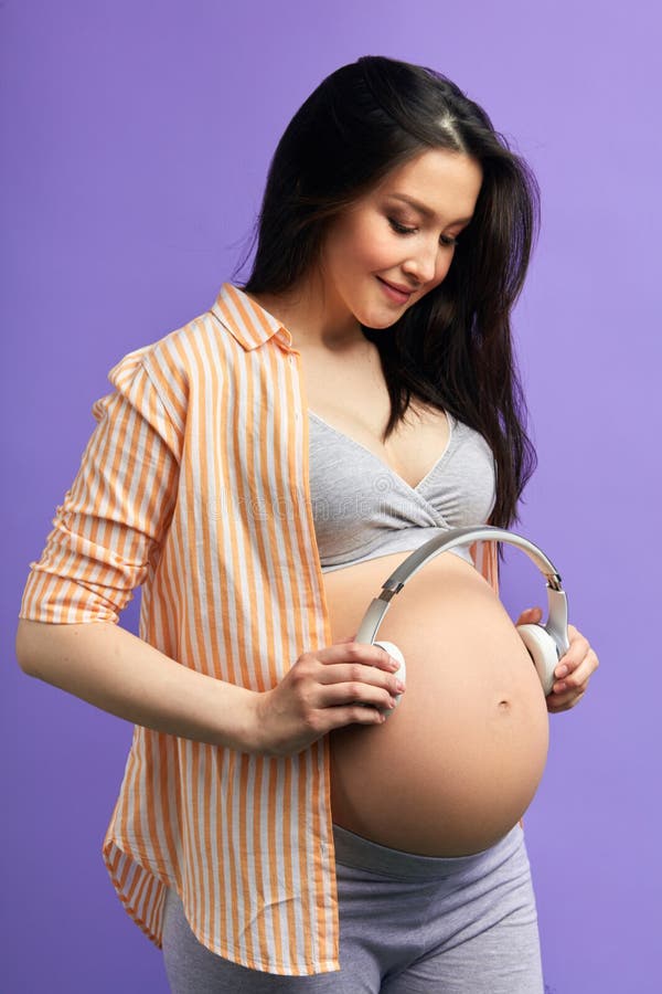 Close-up, Belly Of A Pregnant Young Girl Who Wears A Pink Sweater, Holds  White Headphones On Her Belly, The Baby Listens To Music. The Concept Of  Pregnancy, Motherhood, Preparation And Expectation. Stock