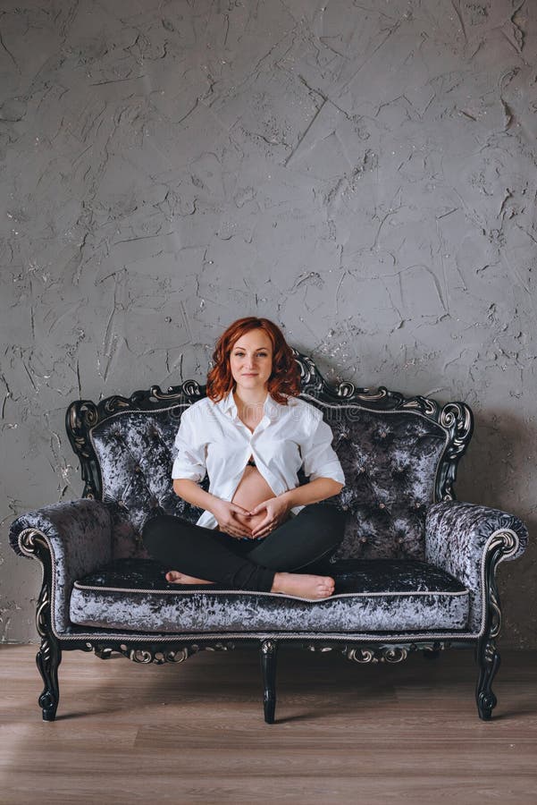 Young Pregnant Woman with Red Hair Sitting on a Gray Sofa in the ...