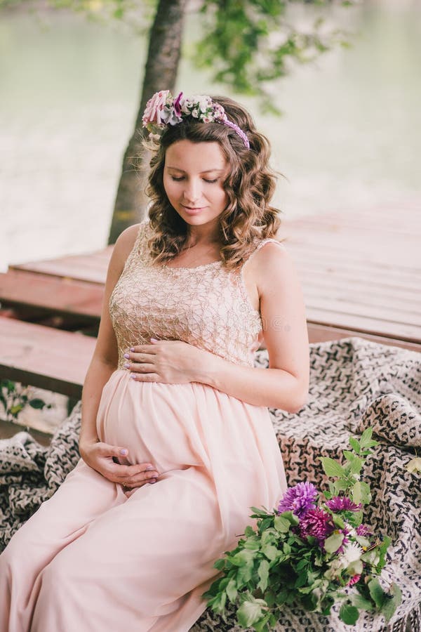 Young pregnant woman sitting near lake