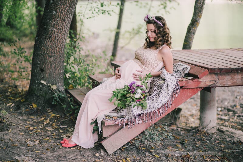 Young pregnant woman sitting near lake