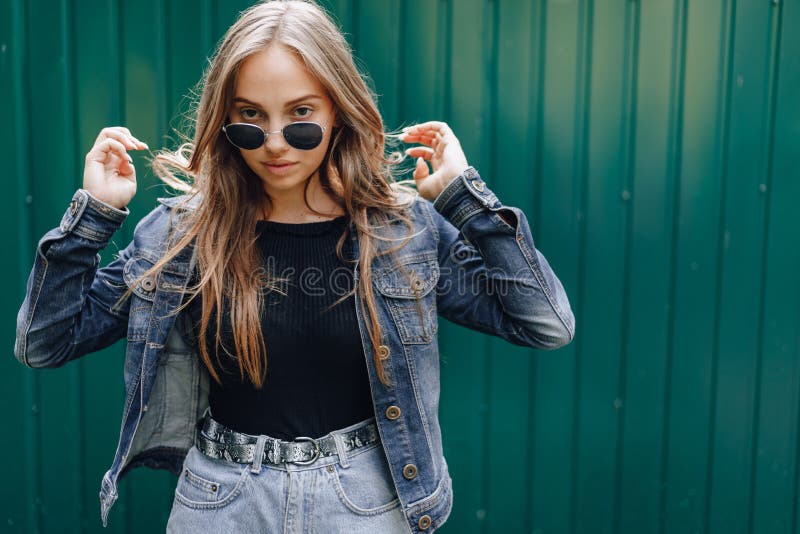 Young pretty attractive girl in denim clothes in glasses on a simple dark green background with place for text